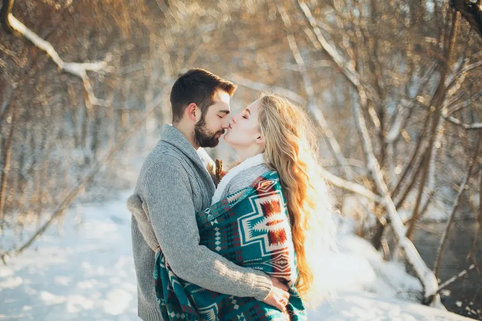 Una pareja se abraza con cariño en un parque nevado, mostrando afecto y complicidad.
