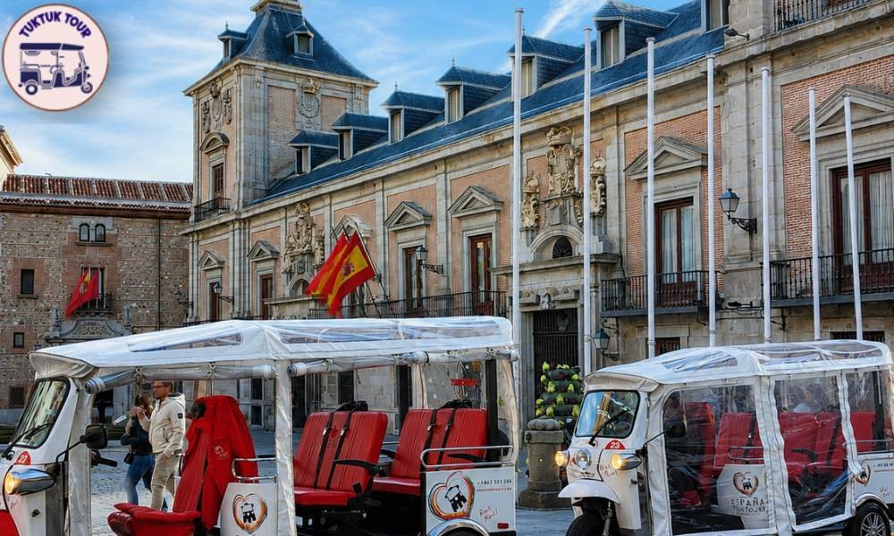 Electric tuk tuk stopped near the Royal Palace of Madrid with a guide pointing out the facade